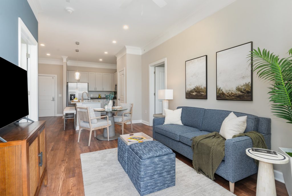 Bright and modern living room with stylish furnishings and open-concept kitchen. Features a comfortable blue sofa, chic dining area, and hardwood floors.