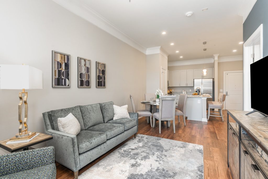 Spacious living and dining area with contemporary design, including a gray sofa, stylish dining chairs, and a fully equipped kitchen with an island.