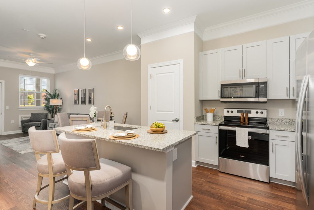 Bright and modern kitchen with granite countertops, stainless steel appliances, and a breakfast bar with cushioned stools. The open-concept layout seamlessly connects to the cozy living area, featuring elegant decor and large windows for ample natural light.