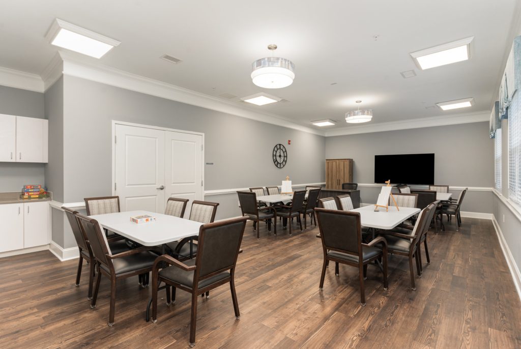 Versatile multipurpose room equipped with multiple tables and a large TV, perfect for meetings, games, and social activities.