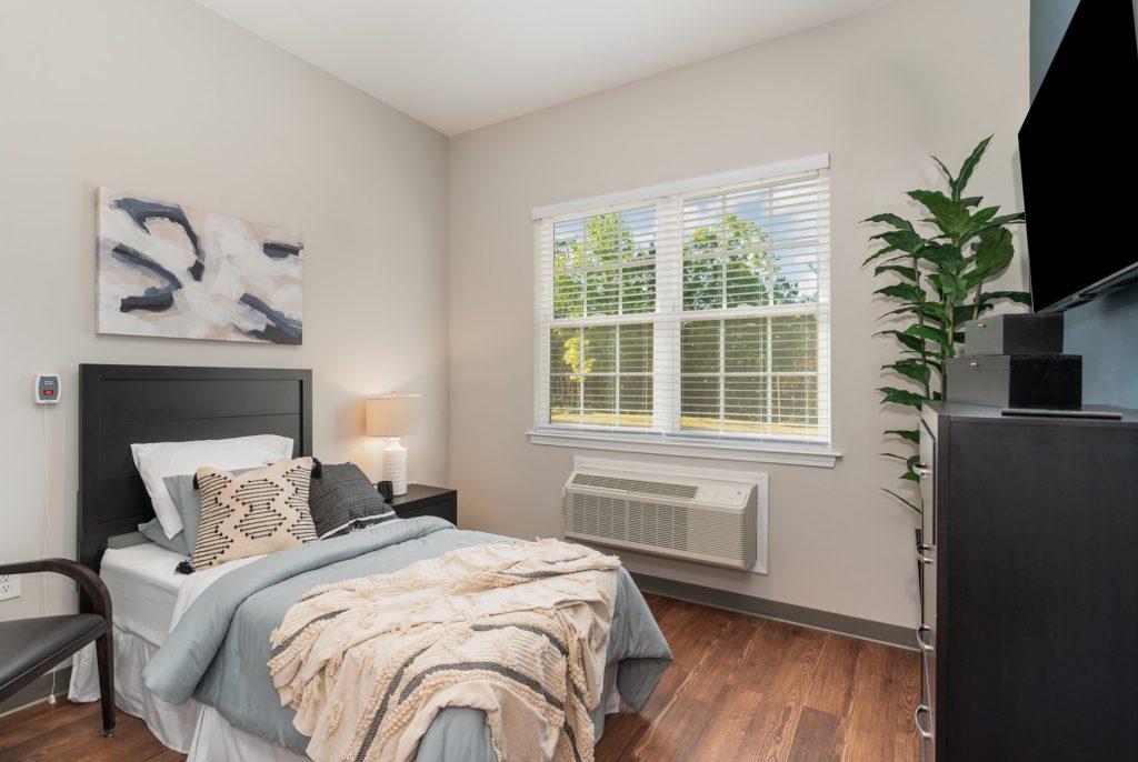 Comfortable bedroom with modern decor, featuring a large window for natural light, a single bed, and stylish furnishings. Perfect for a restful retreat.
